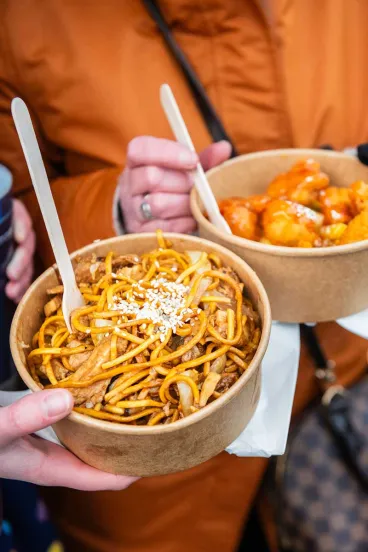 Hands holding paper bowls with takeout Chinese food
