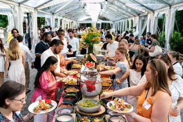 A crowd of people making plates of food for themselves at a catered buffet